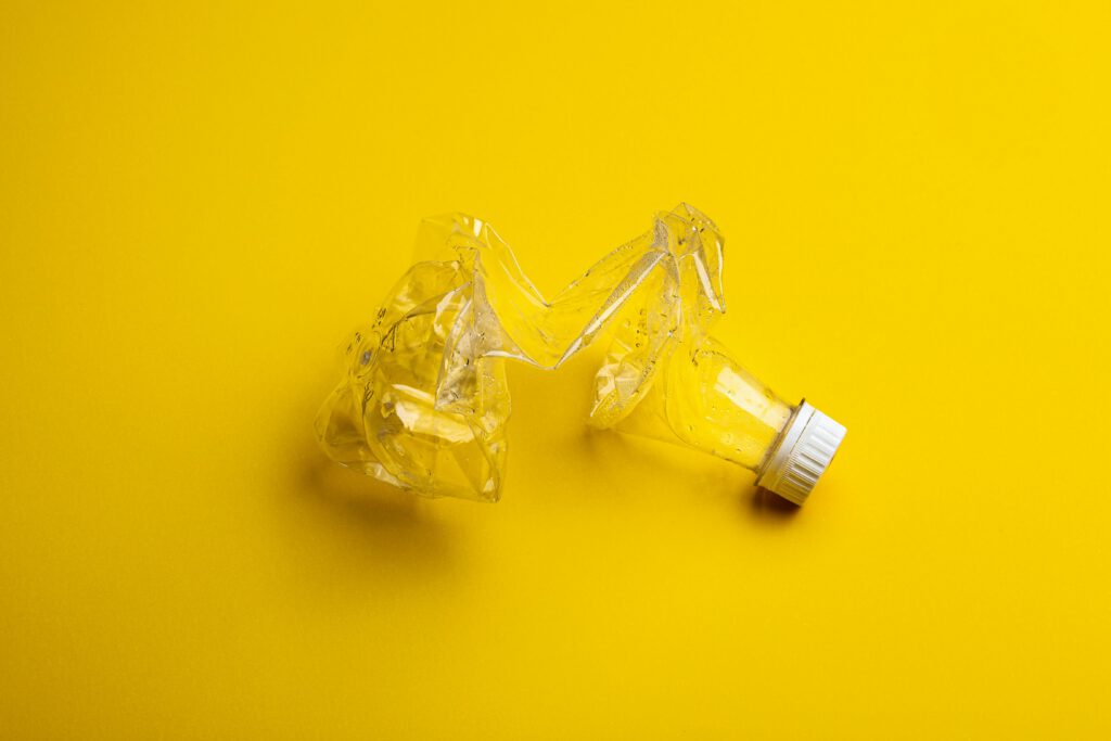A crumpled plastic bottle against a bright yellow backdrop, highlighting recycling themes.